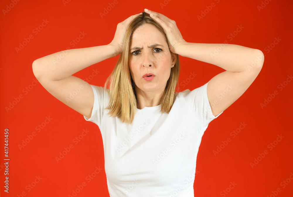 Obraz premium Shocked amazed young woman with hands on head standing over red background