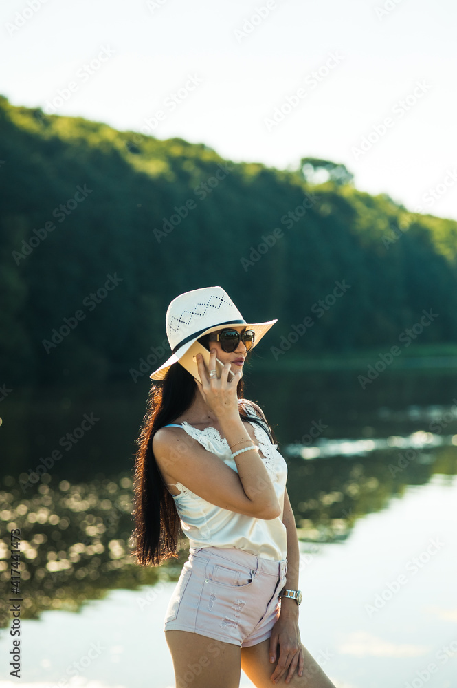 Sexy girl talking on the phone in the park.Gorgeous slender brunette talking on the phone by the lake.Smiling woman talking outdoors.