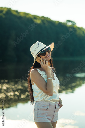 Sexy girl talking on the phone in the park.Gorgeous slender brunette talking on the phone by the lake.Smiling woman talking outdoors.