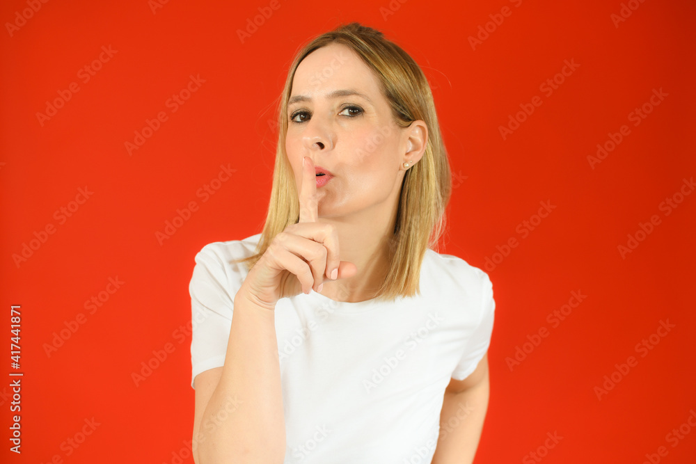 Portrait of beautiful woman standing over isolated red background asking to be quiet with finger on lips. Silence and secret concept. Portrait of beautiful woman standing over isolated red background asking to be quiet with finger on lips. Silence and secret concept.