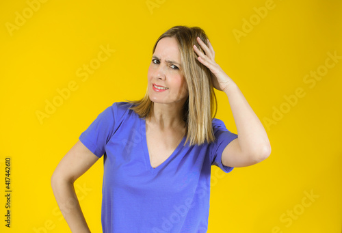 Shocked amazed young woman with hand on head standing over yellow background