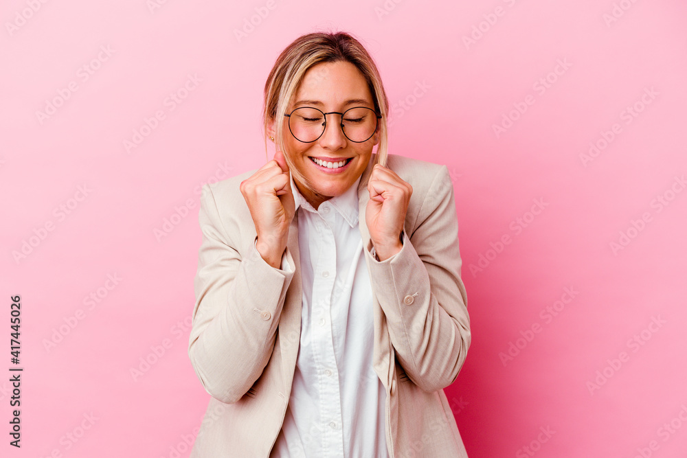 Young caucasian mixed race business woman isolated on pink background raising fist, feeling happy and successful. Victory concept. Young caucasian mixed race business woman isolated on pink background raising fist, feeling happy and successful. Victory concept.