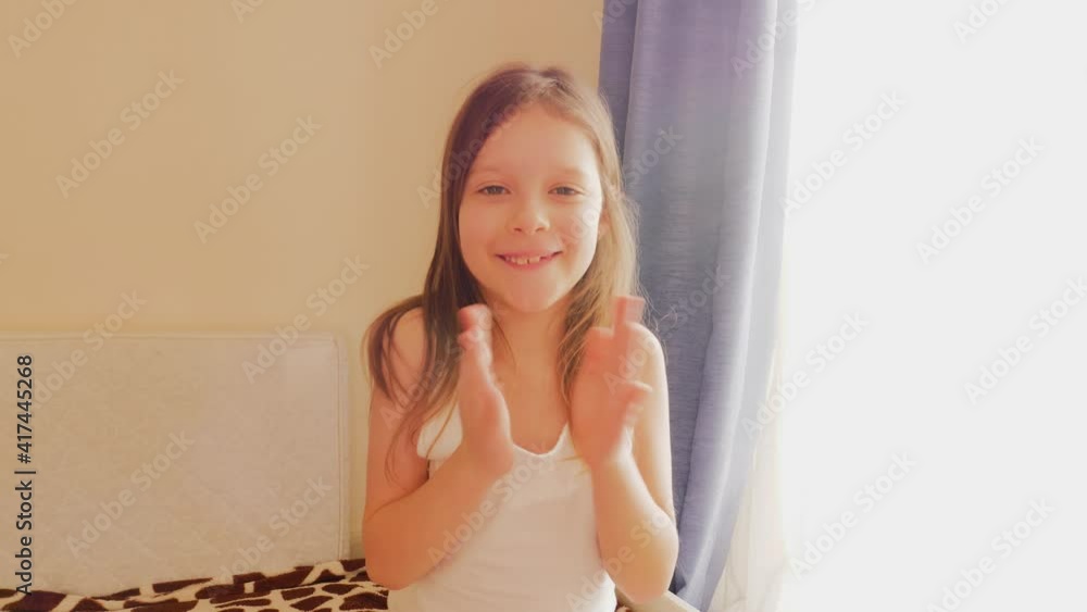 Cute child girl rejoice happy to hear something clapping hands and smile sitting near bright window Cute child girl rejoice happy to hear something clapping hands and smile sitting near bright window