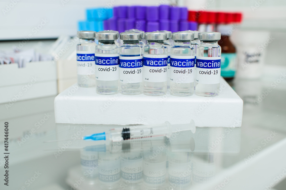 glass medical jars with the inscription covid-19 vaccine on the glass surface in the clinic. glass medical jars with the inscription covid-19 vaccine on the glass surface in the clinic.