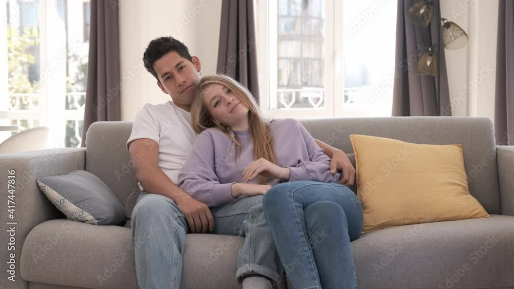 Portrait of young couple smiling and looking at the camera while sitting on the couch at home. Portrait of young couple smiling and looking at the camera while sitting on the couch at home.
