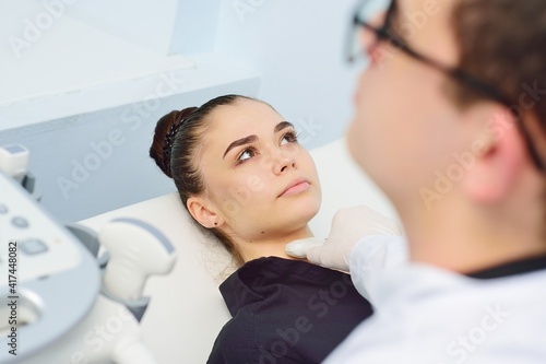 a doctor in a modern diagnostic clinic examines the thyroid gland of a patient of a young attractive woman on an ultrasound machine. Prevention of thyroid cancer.