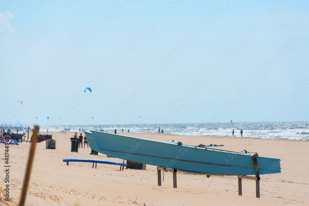 Close up of a blue catamaran boat on a metal stand on the beach of Zandvoort in the Netherlands. kite of surfers viisible in the background
