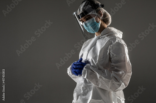 Healthcare concept. Doctor woman in white hazmat suit  glasses and respirator mask standing isolated on gray background with copy space