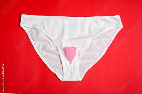 white panties on a red background with a pink silicone menstrual cup. the concept of menstruation and eco-friendly reusable pads replaced