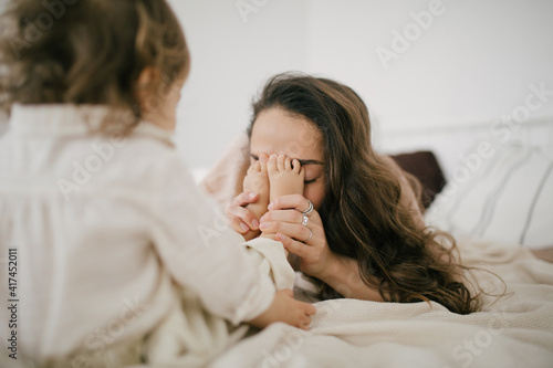 Young mother and her little daughter having fun in a bedroom, they playing, laughing and hugging. Happy family concept.