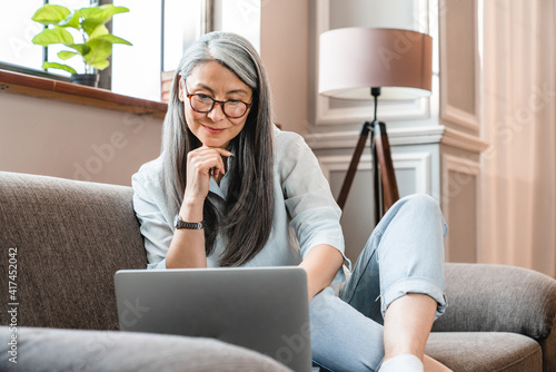 фотографія Cheerful mature caucasian woman working on laptop in the living room