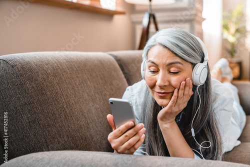 Cheerful mature caucasian woman listening to the music on the sofa