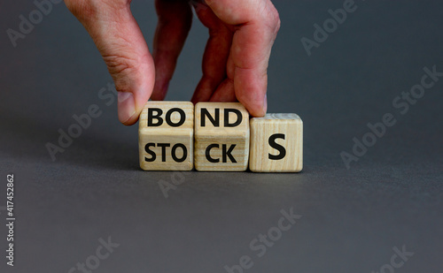 Stocks vs bonds symbol. Businessman turns wooden cubes and changes the word 'stocks' to 'bonds'. Beautiful grey background, copy space. Business and stocks vs bonds concept.