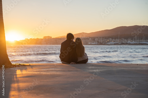 A couple embracing each other with a beautiful sunset in the background by the sea in Palma de Mallorca, Spain