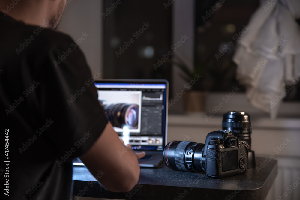 A digital professional camera on the table near the photographer who works at the laptop.