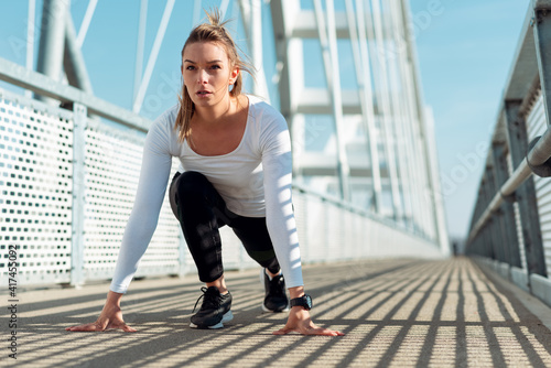 Athlete woman in running start pose on the bridge. Sunny day, blurry background