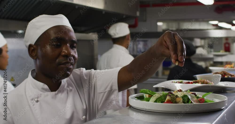 African american male chef garnishing dish and similing in restaurant kitchen African american male chef garnishing dish and similing in restaurant kitchen