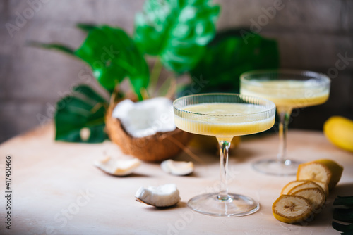 banana cocktail with coconut milk in a glass on light beige background with palm leaves