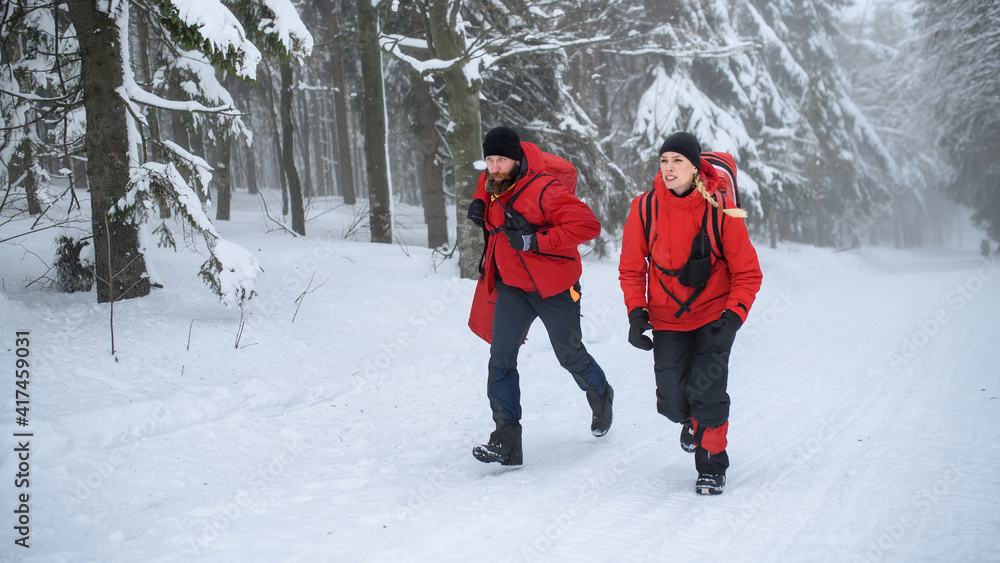 Paramedics from mountain rescue service running outdoors in winter in forest.