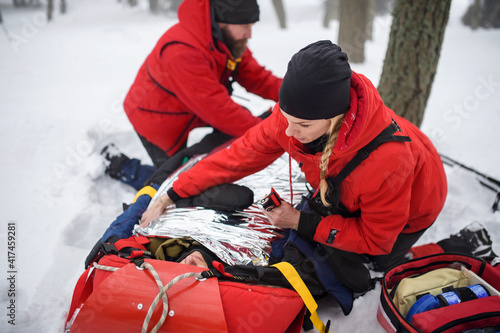 Mountain rescue service provide operation outdoors in winter in forest, injured person in stretcher.