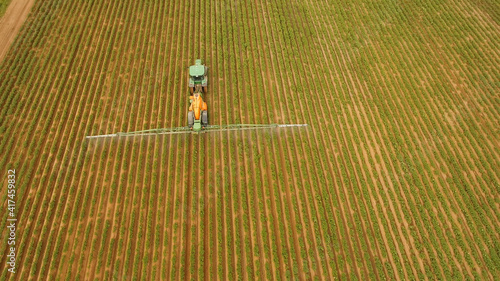 Aerial view tractor spraying the chemicals on the large green field. Spraying the herbicides on the farm land. Treatment of crops against weeds.