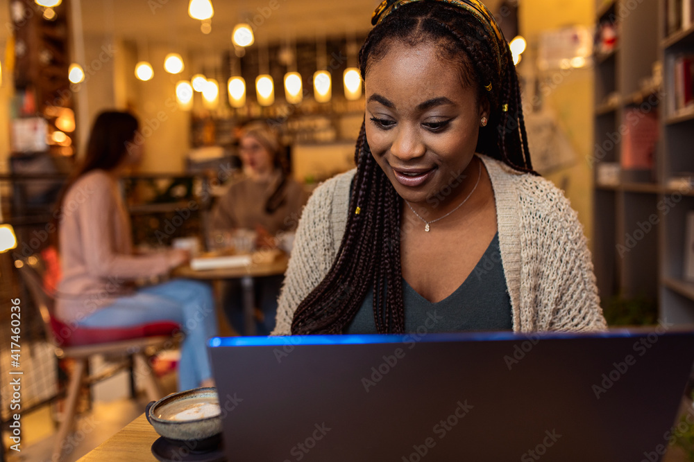 Fototapeta premium Portrait of young African woman using laptop in coffee shop
