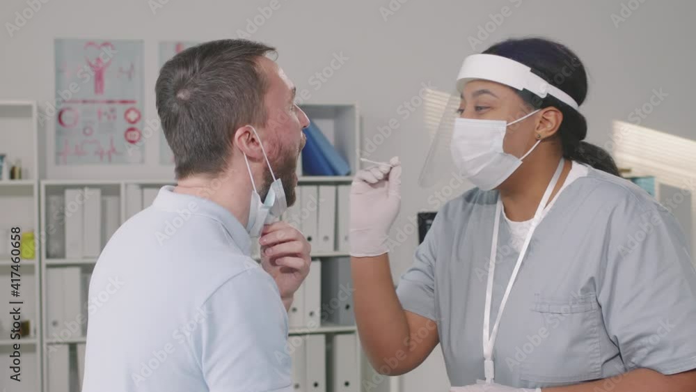 Waist-up shot of african american nurse in protective clothing and face shield taking throat swab from male patient for coronavirus test Waist-up shot of african american nurse in protective clothing and face shield taking throat swab from male patient for coronavirus test
