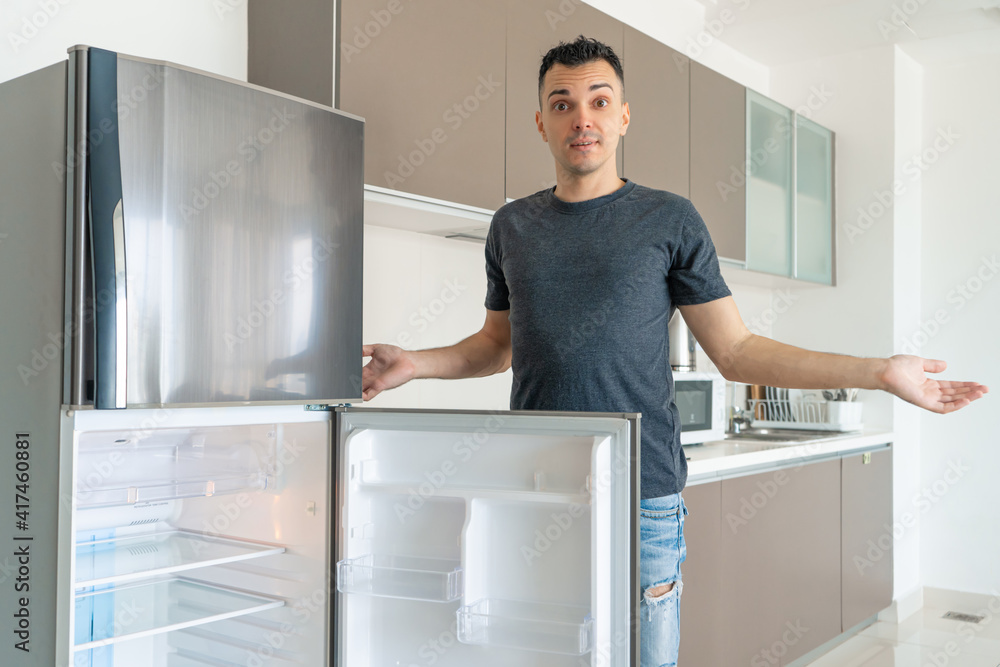 The guy is sad near the empty refrigerator without food. Food delivery service advertisement The guy is sad near the empty refrigerator without food. Food delivery service advertisement