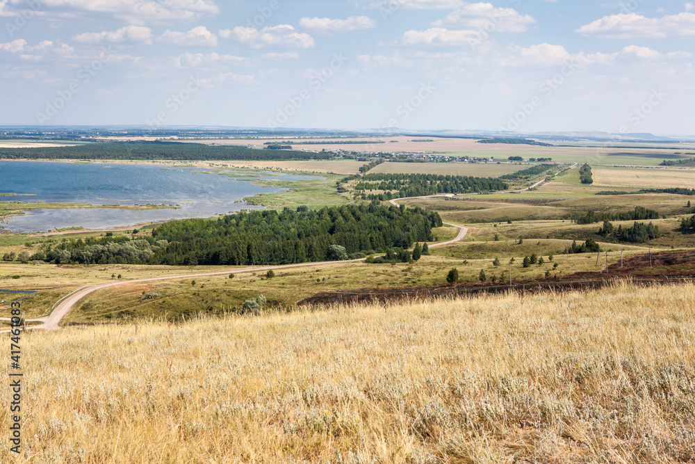 Rural road crossing hills and countryside, panorama. The Aslikul lake, the Republic of Bashkortostan, Russia