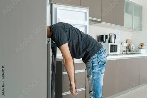 On a hot day, the guy cools with his head in the refrigerator. Broken air conditioner photo