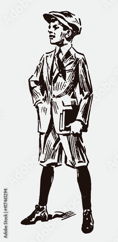 Standing schoolboy from early 20th century wearing knickerbockers and cap, holding two books