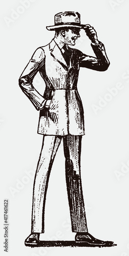 Standing young man from the early 20th century wearing suit and touching his hat