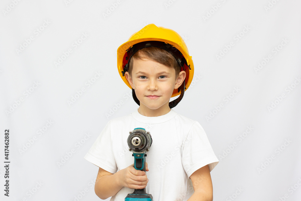 Boy in yellow helmet is drilling Home renovation. Teenager boy learning to drill. Instrument and tool for remodeling. Male worker with machine.