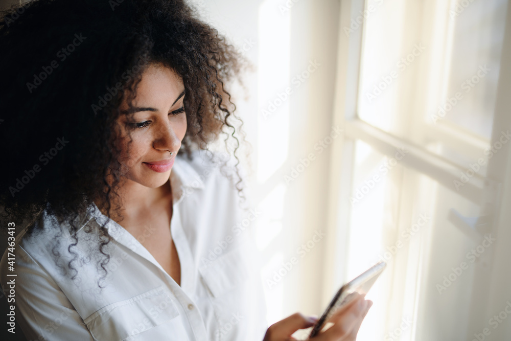 Portrait of young woman on window sill indoors at home, using smartphone. Portrait of young woman on window sill indoors at home, using smartphone.