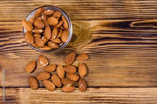 Glass bowl with the peeled almond nuts on wooden table. Top view photo