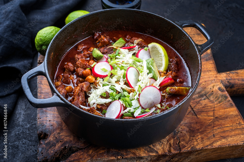 Traditional slow cooked Mexican pozole rojo as top view in a modern design cast-iron roasting dish on an old rustic wooden board