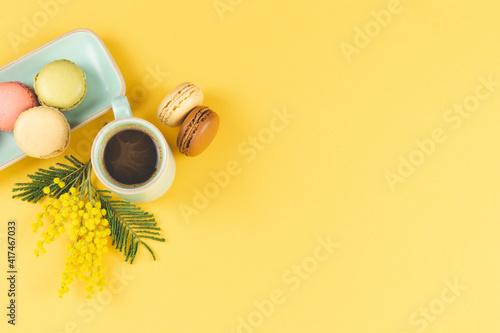 Coffee mug with macarons and mimosa flowers on yellow background. Copy space. © castellanos80