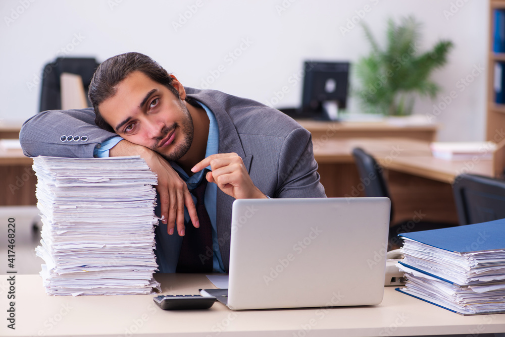 Young male employee unhappy with excessive work in the office Young male employee unhappy with excessive work in the office