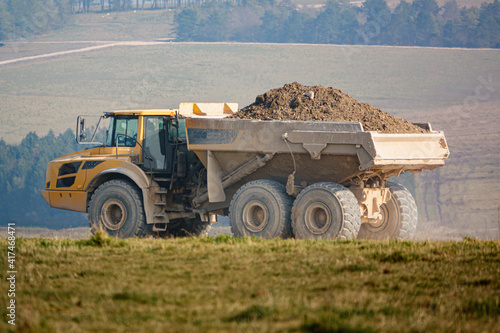 yellow Volvo A40E articulated dump truck earth mover fully laden with 25 tonne load driving across open countryside Wiltshire UK