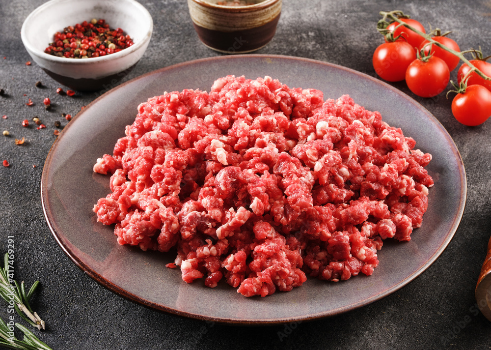 Homemade minced meat in a grey bowl over dark background or stone background with ingredients for making. Homemade minced meat in a grey bowl over dark background or stone background with ingredients for making.