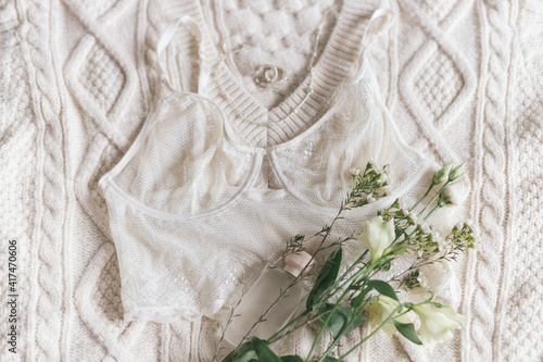 Stylish lingerie, perfume, jewelry and spring flowers on sweater. Soft trendy image. Fragrance