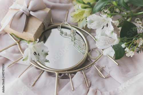 Stylish gift, modern jewelry, spring flowers on boho mirror on soft fabric. Gentle feminine image
