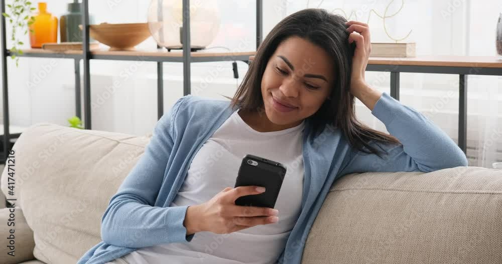 Woman text messaging using mobile phone on sofa at home Woman text messaging using mobile phone on sofa at home