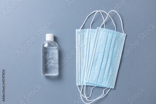 Medical protective, blue face masks, sanitizer gel, on gray background, close-up, flatly, minimal style, copy space. Hygiene concept, personal protectional gear, prevention of spread of infections. photo