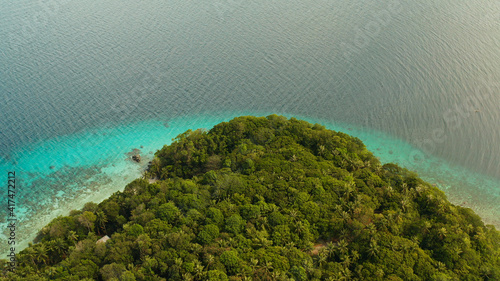 Coastline with forest and palm trees, coral reef with turquoise water, aerial view. Sea water surface in lagoon and coral reef. Seascape of tropical island covered wgreen forest Camiguin, Philippines photo