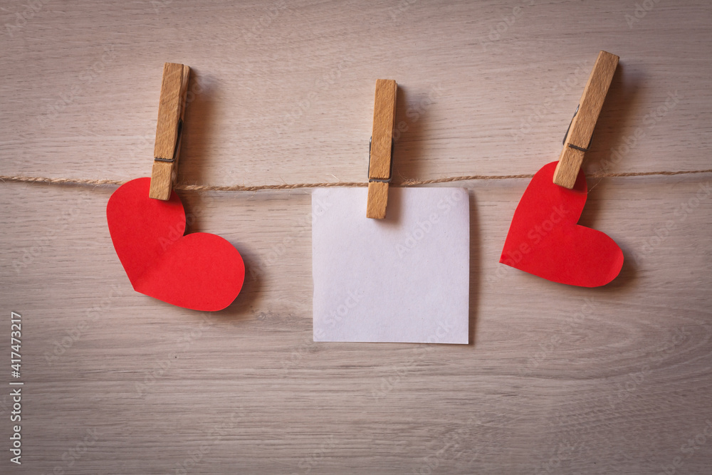 Fototapeta premium Clothespins with blank sheets of paper hanging on wooden background with hearts.