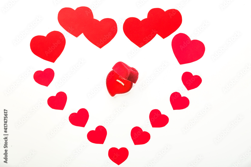 A large heart made of paper hearts laid out on a white background in the middle of a red box with a gold ring.