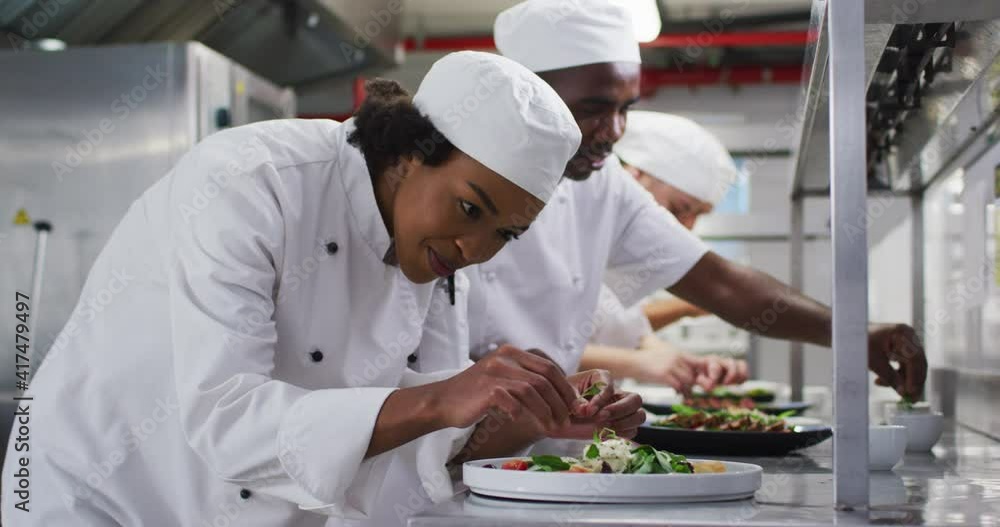 Diverse group of chefs garnishing dishes and similing in restaurant kitchen Diverse group of chefs garnishing dishes and similing in restaurant kitchen