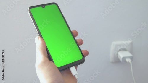 Charging charge mobile phone, smartphone. Man holds a cell phone in his hand on a background of walls and sockets. Connecting the charger USB C. Charg device process. Green screen