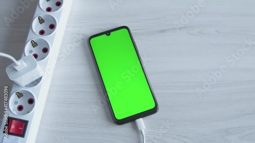 Charging mobile phone, smartphone. Man put cell phone charge on extension cord socket on wooden background. Connecting the charger USB C. Charg device process.Green screen